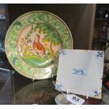 An 18th Century Delft style tile decorated crouching dog (framed), and a pottery plate decorated