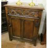 An oak cupboard with single panelled door and carved drawer