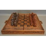 A Bali Indonesian Carved Figural Chess Set with carved and inlaid folding chess board
