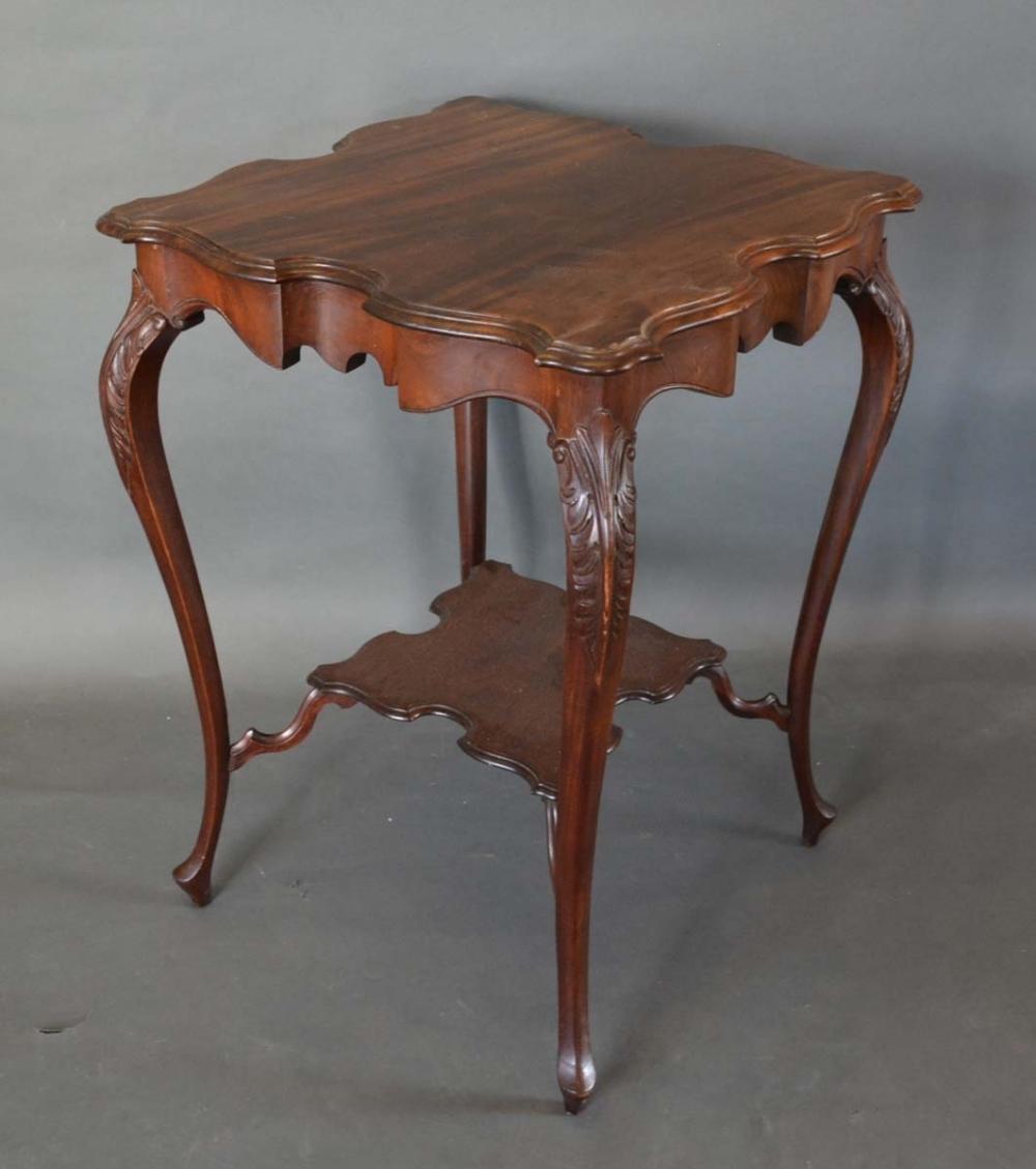 An Edwardian Mahogany Two Tier Occasional Table with a shaped moulded top raised upon carved