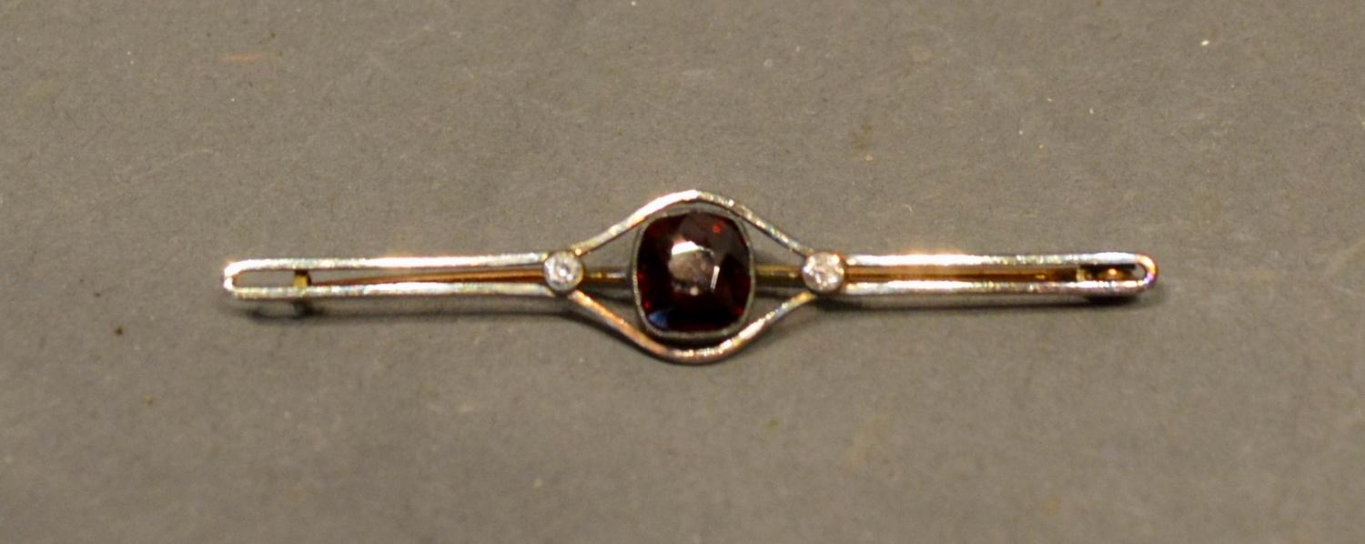 A White Metal Bar Brooch set with a central garnet flanked by diamonds