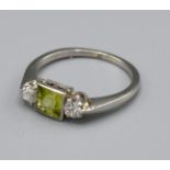A Platinum Diamond and Peridot Ring with Central Square Peridot flanked by two diamonds within a