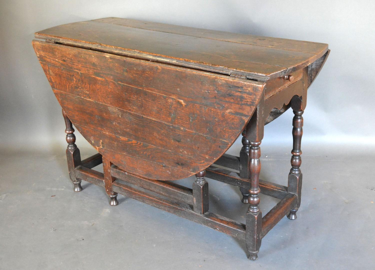A George III Oak Oval Gate Legged Dining Table with a frieze drawer raised upon turned legs with