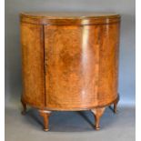 An Early 20th Century Burr Walnut Demi-Lune Side Cabinet, the moulded crossbanded top above a