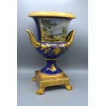 A Paris Porcelain Style Urn hand painted with a reserve depicting a landscape upon a cobalt blue and