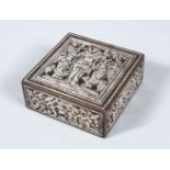 A 19TH CENTURY INDIAN SILVERED LIDDED BOX, with embossed decoration of a deity, 8cm square.