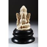 A CARVED IVORY FOUR-FACED SEATED MALE FIGURE, on a turned wood base, 11cm high.