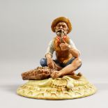 A CAPODIMONTE GROUP, a man seated by a basket of fish, smoking his pipe. 9ins wide.