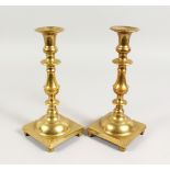 A PAIR OF HEAVY BRASS CANDLESTICKS, with square bases. 9.75ins high.