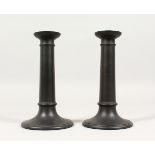 A PAIR OF PLAIN WEDGWOOD BLACK BASALT CIRCULAR CANDLESTICKS. Impressed WEDGWOOD. 7ins high.