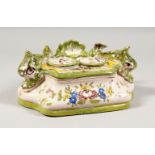 A FAIENCE POTTERY TWO BOTTLE INKSTAND, painted with flowers and mounted with dolphins. 9ins long.