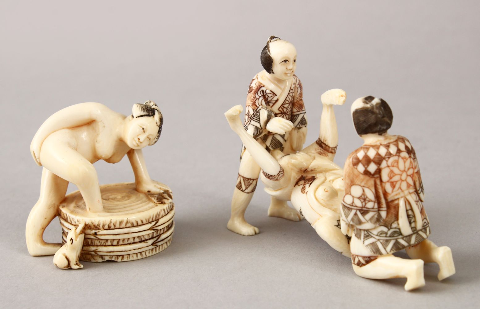 A JAPANESE LATE MEIJI PERIOD CARVED EROTIC IVORY NETUSKE & EROTIC TRIO, the netsuke of a lady over a