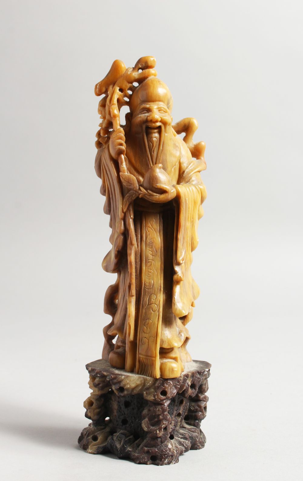 A GOOD 19TH / 20TH CENTURY CHINESE CARVED SOAPSTONE FIGURE OF SHOU LAO, stood on a carved stone base