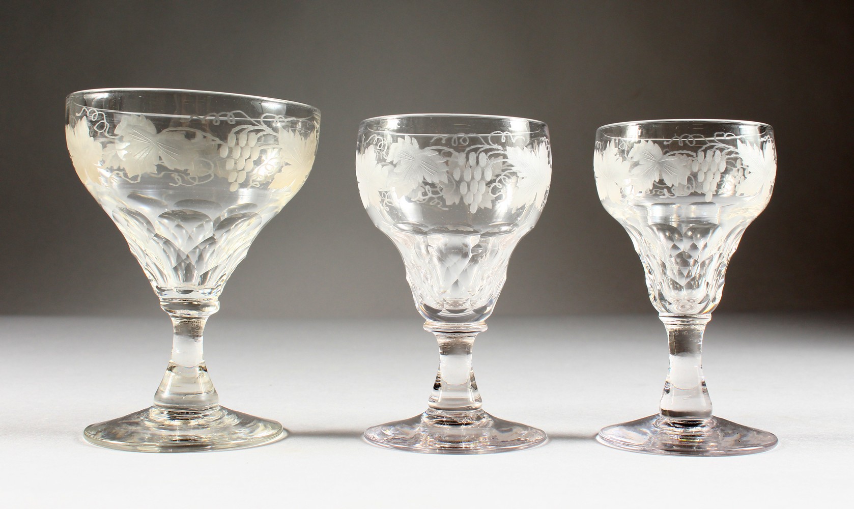 A SUITE OF GLASSWARE, etched with fruiting vines, comprising six large wine glasses and twelve other