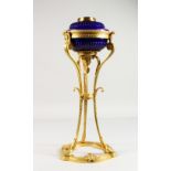 AN EMPIRE ORMOLU LAMP, with blue glass reservoir, on three hoof feet. 20ins high.