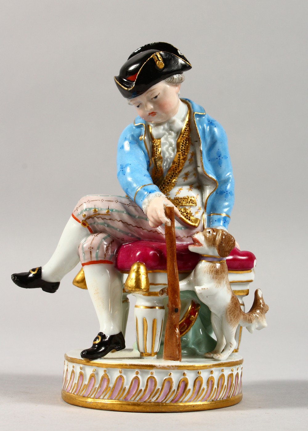 A 19TH CENTURY MEISSEN PORCELAIN FIGURE OF A BOY, seated on a stool holding a gun, dog by his