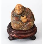 A CHINESE CARVED SOAPSTINE FIGURE OF A SEATED LUOHAN, In a seated position holdiong a bowl, with his