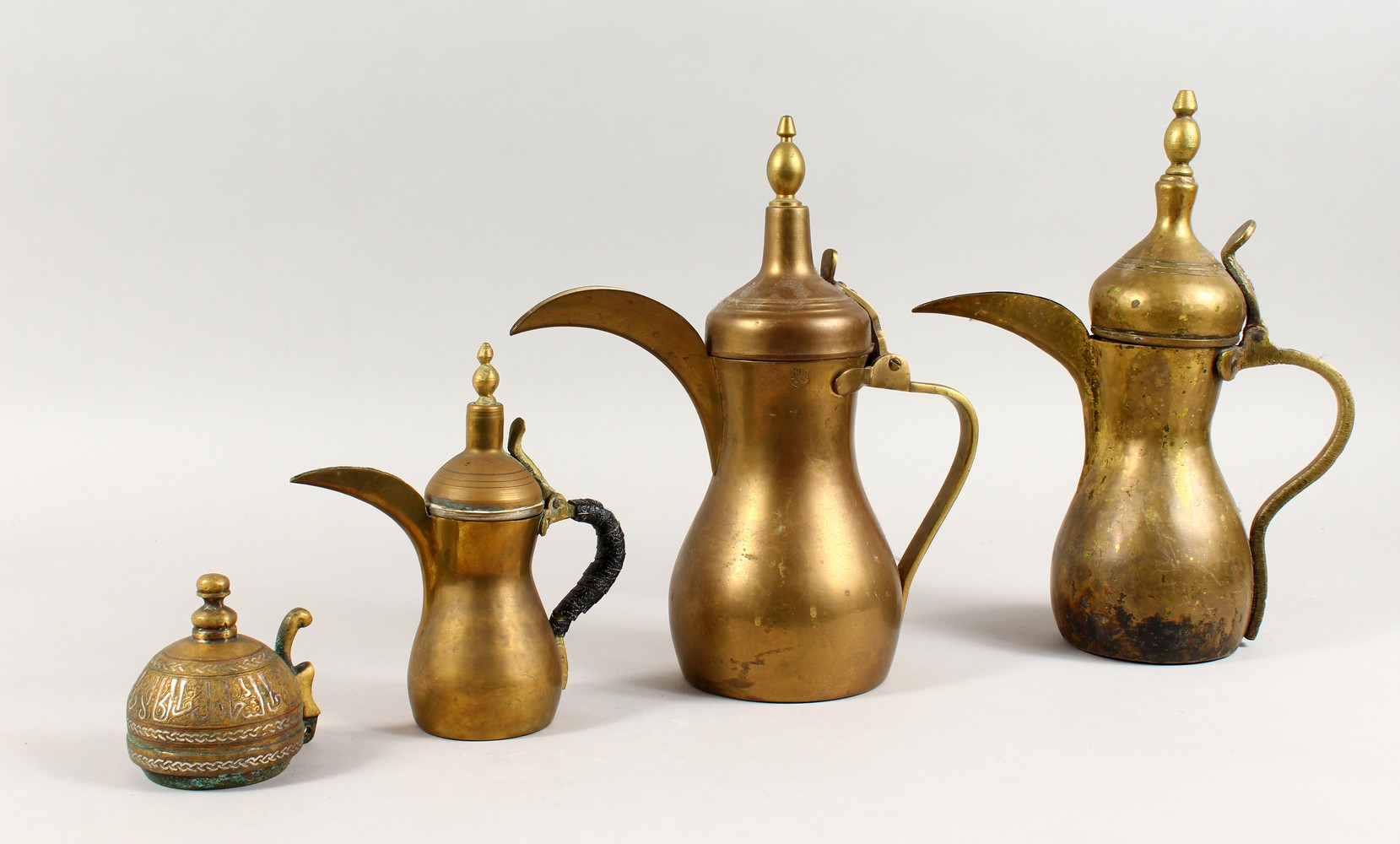 A SET OF THREE ANTIQUE ARABIC BRASS COFFEE POTS SIGNED DALLAH & AN ISLAMIC SILVER INLAID LID, coffee