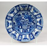 A BLUE AND WHITE TIN GLAZE CIRCULAR DISH, with a vase of flowers and emblems. 13.5ins diameter.