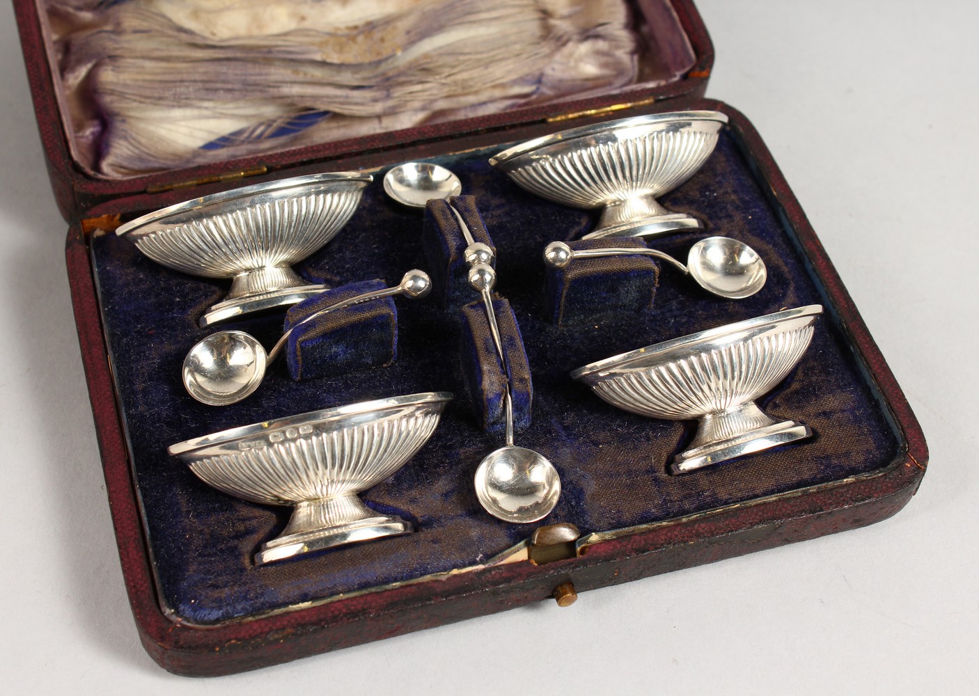 A CASED SET OF FOUR SMALL PEDESTAL SALTS WITH SPOONS.