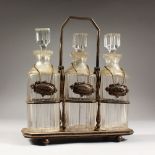 A GOOD THREE BOTTLE CUT GLASS TANTALUS, with three whisky decanters & stoppers and wine labels.