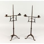 TWO 18TH/19TH CENTURY WROUGHT IRON CANDLESTICKS, on tripod bases. 23ins high.
