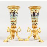 A PAIR OF ORMOLU AND CHAMPLEVE ENAMEL VASES, each of trumpet form on three legs with claw feet. 6ins