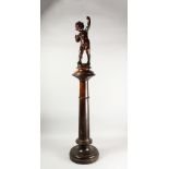 A GOOD CARVED WOOD PUTTI, standing on a circular plinth.