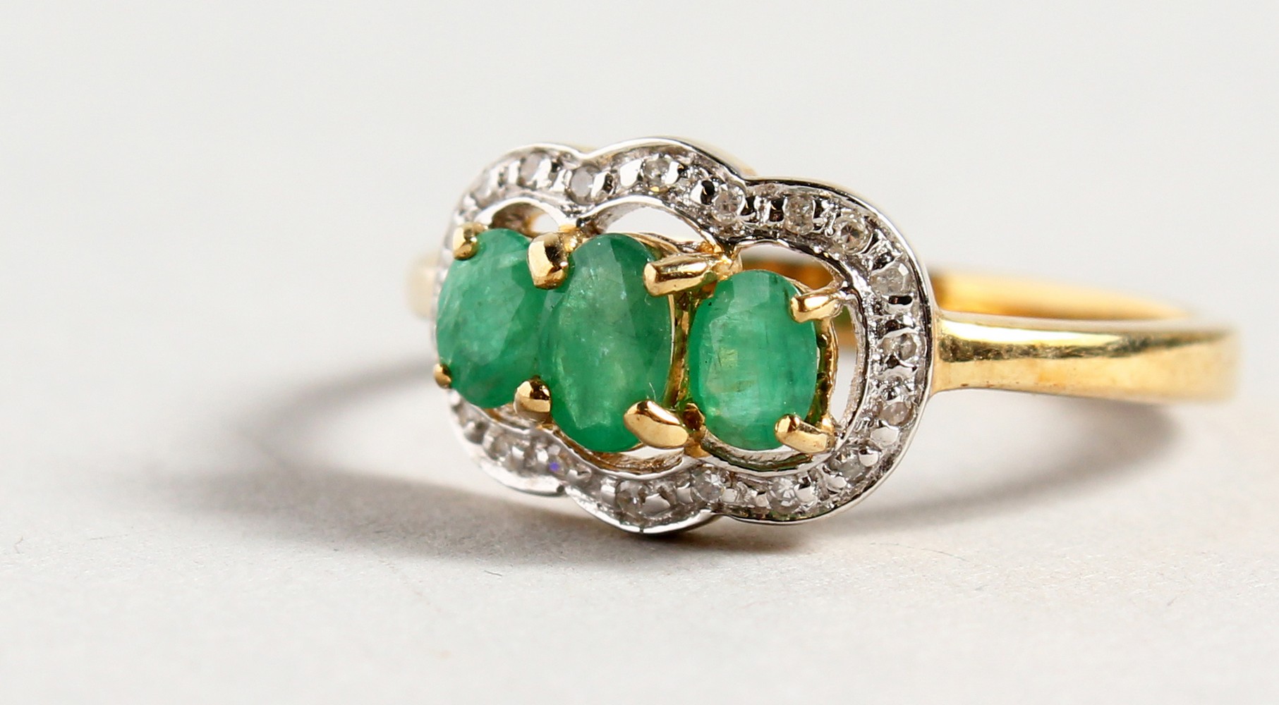 A 9CT GOLD THREE STONE EMERALD AND DIAMOND RING.