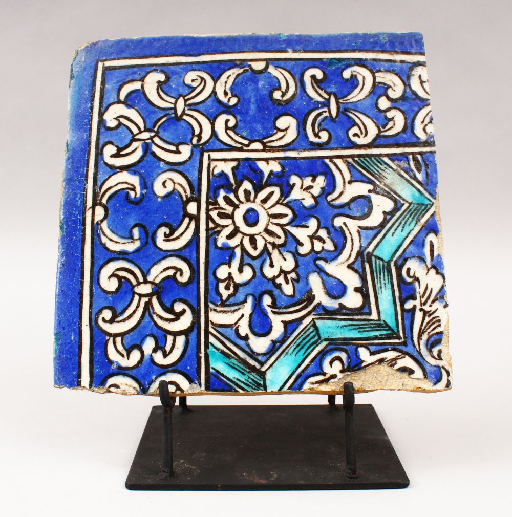 A 19TH CENTURY PERSIAN QAJAR BLUE AND WHITE CORNER TILE on a metal stand, tile 21.5cm x 21.5cm.