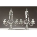 A PAIR OF GLASS TWO BRANCH CANDLESTICKS, with prism drops, on a circular base. 21ins high.