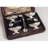 A CASED SET OF FOUR SMALL PEDESTAL SALTS WITH SPOONS.