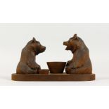 A BLACK FOREST STYLE CARVED GROUP OF TWO BEARS, each seated by a bowl. Label to the underside. 12ins