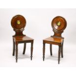 A GOOD PAIR OF REGENCY MAHOGANY HALL CHAIRS, the circular backs with painted crests, solid seats