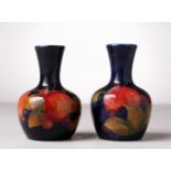 A NEAR PAIR OF SMALL MOORCROFT POTTERY BULBOUS VASES, pomegranate and fruit, blue ground. W.