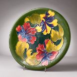 A LARGE MOORCROFT CIRCULAR GREEN GROUND PLATTER, "Hibiscus". Impressed MOORCROFT. Script WM. 12ins