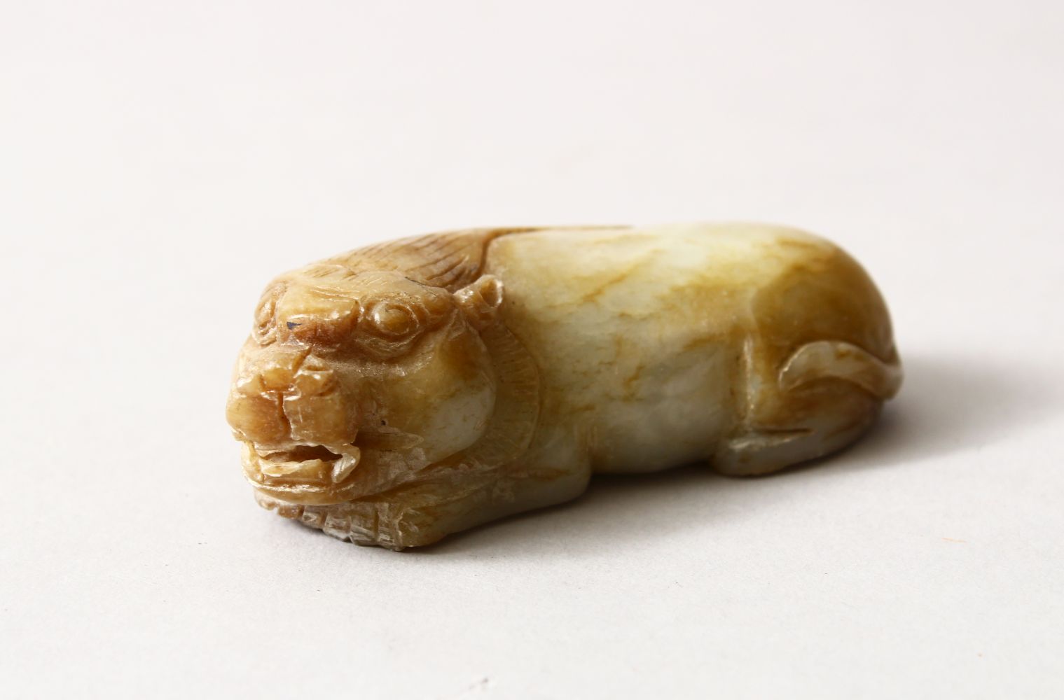 A CHINESE CARVED JADE / HARD STONE FIGURE OF A RECUMBENT KYLIN, 7.5cm.