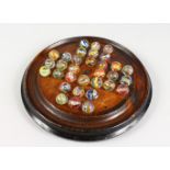 A WOODEN SOLITAIRE BOARD WITH AIR TWIST MARBLES. 10.5ins diameter.