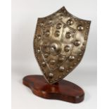 AN IMPRESSIVE 19TH CENTURY MEDIEVAL STYLE EMBOSSED STEEL SHIELD, mounted on an oak base. Shield: