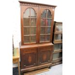 A teak cupboard bookcase with a pair of glazed doors above a pair of panelled doors on turned feet.