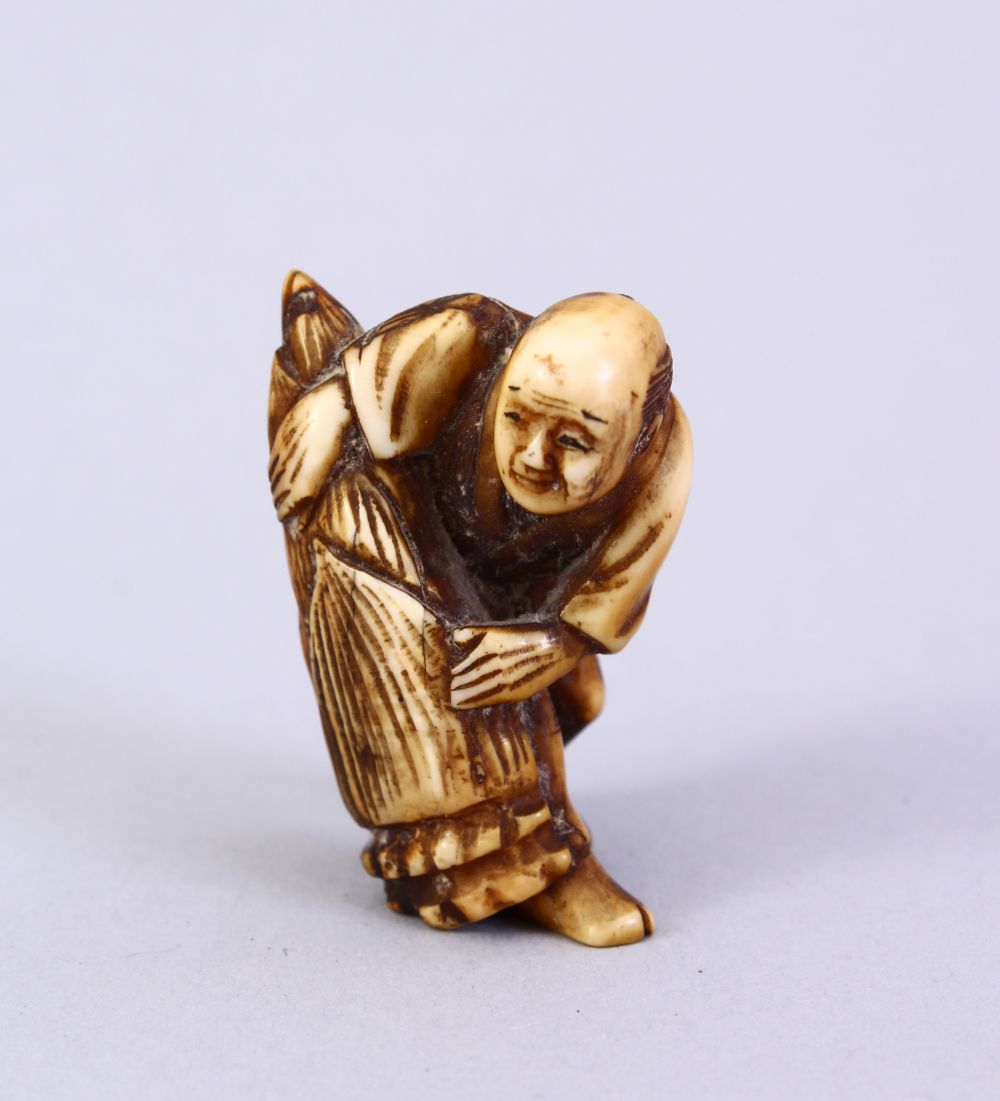 A JAPANESE MEIJI PERIOD CARVED IVORY NETSUKE, the figure holding a tied parcel, signed to side, 3.