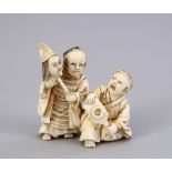 A JAPANESE MEIJI PERIOD CARVED IVORY OKIMONO OF TWO BOYS, one holding a mask, the other a small bat,