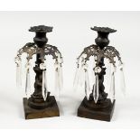 A PAIR OF BRONZE LUSTRE CANDLESTICKS, with cut glass prism drops, on square bases. 9ins high.