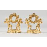 A SMALL PAIR OF GILT CHERUB MENU HOLDERS.