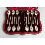 A SET OF TWELVE ENGRAVED TEASPOONS AND SUGAR TONGS in a leather case. London 1930.