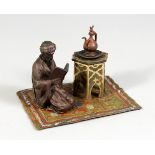 A COLD PAINTED BRONZE GROUP, ARAB READING A BOOK, on a carpet. 5.5ins long.