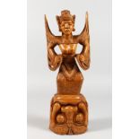 AN UNUSUAL THAI CARVED WOOD FIGURE, carved as a standing winged semi-nude female, on an upturned