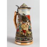 A GERMAN POTTERY LIDDED JUG, decorated with merrymaking figures. 10ins high.