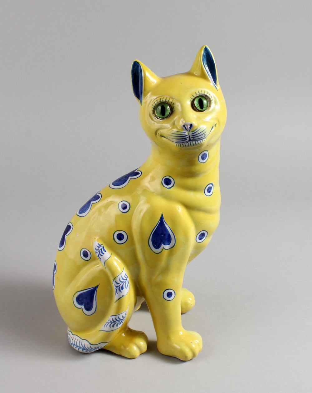 AFTER GALLE, A GOOD POTTERY SEATED CAT, yellow ground with blue painted stylised emblems and green