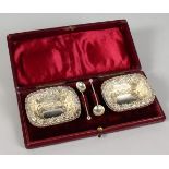 A SET OF FOUR EMBOSSED SILVER SALTS, with two spoons, boxed.